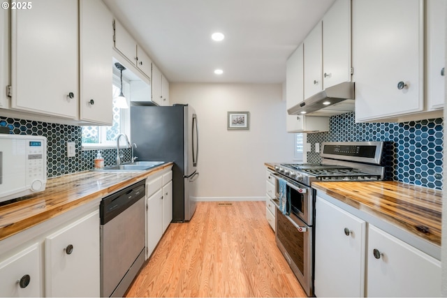 kitchen featuring under cabinet range hood, butcher block counters, a sink, stainless steel appliances, and white cabinets