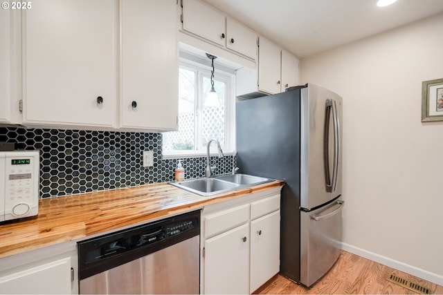 kitchen with a sink, stainless steel appliances, white cabinetry, and wood counters