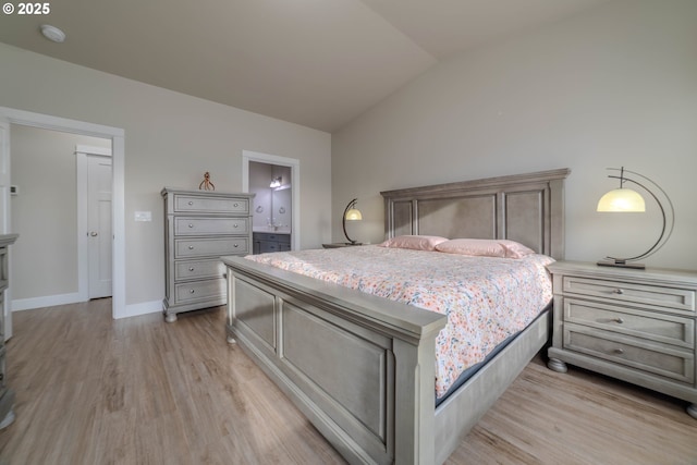 bedroom featuring light wood-type flooring, ensuite bath, and lofted ceiling