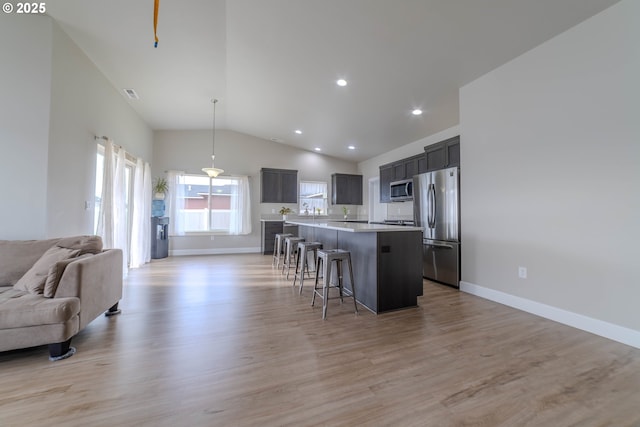 kitchen with light hardwood / wood-style flooring, hanging light fixtures, a kitchen island, appliances with stainless steel finishes, and a kitchen breakfast bar