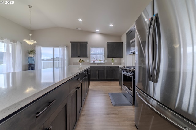 kitchen with a wealth of natural light, stainless steel appliances, lofted ceiling, and hanging light fixtures