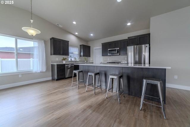 kitchen with appliances with stainless steel finishes, a breakfast bar, decorative light fixtures, and a kitchen island