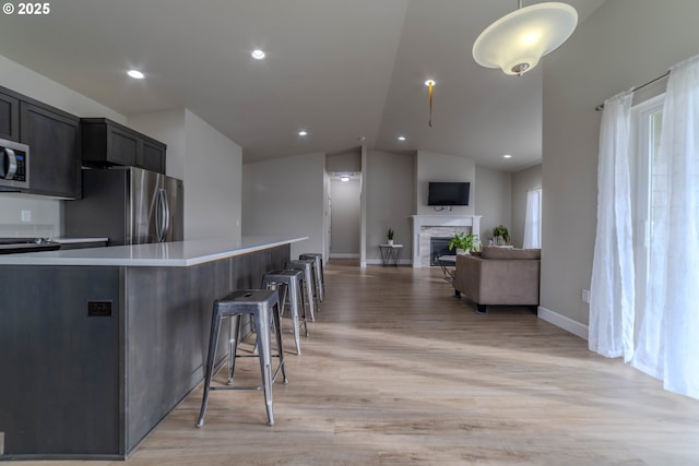 kitchen with decorative light fixtures, lofted ceiling, light wood-type flooring, a breakfast bar area, and appliances with stainless steel finishes