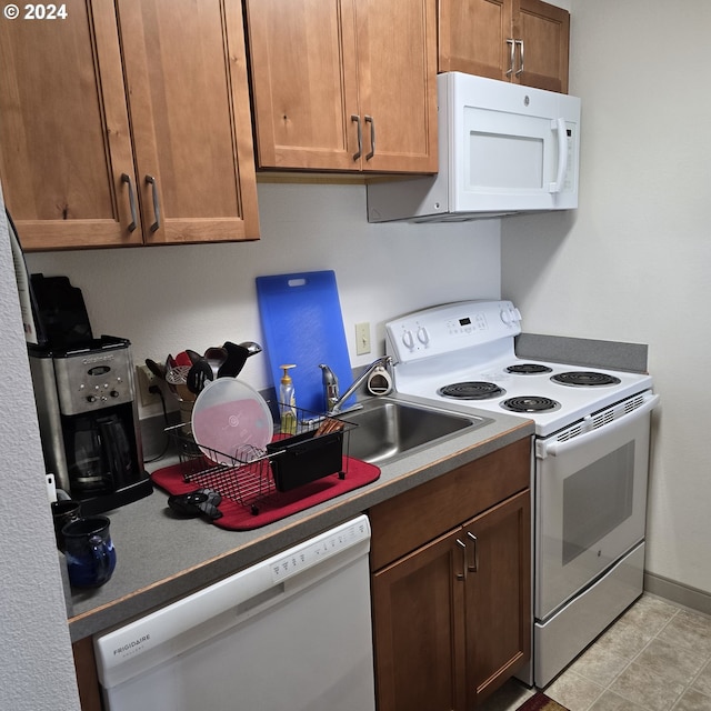 kitchen with brown cabinetry, a sink, white appliances, and baseboards