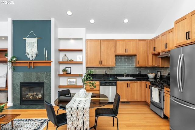 kitchen with stainless steel appliances, sink, a tiled fireplace, light hardwood / wood-style flooring, and backsplash