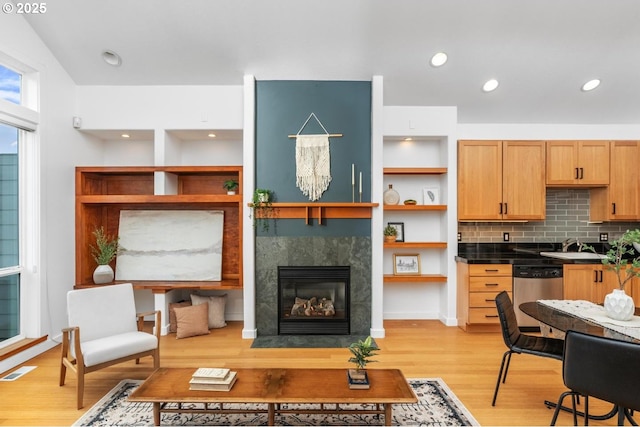 kitchen with stainless steel dishwasher, tasteful backsplash, light wood-type flooring, a fireplace, and sink