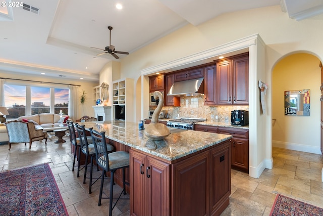 kitchen with tasteful backsplash, a kitchen island, light stone countertops, a breakfast bar, and ceiling fan