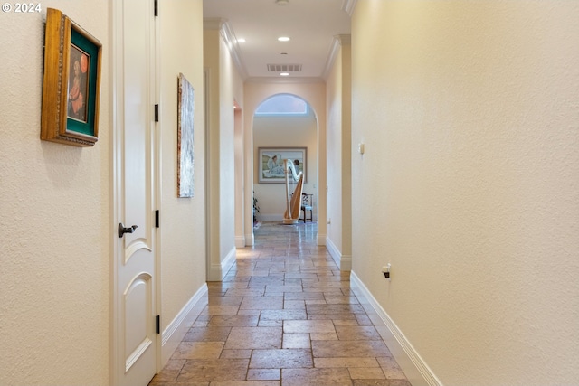 hallway with baseboards, visible vents, crown molding, and stone tile floors