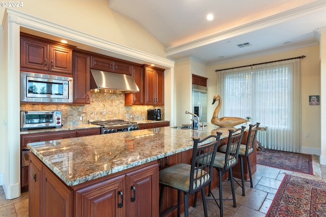 kitchen with a kitchen island with sink, built in appliances, stone tile floors, and exhaust hood