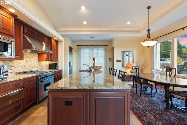 kitchen featuring a kitchen island with sink, a tray ceiling, stainless steel appliances, pendant lighting, and exhaust hood