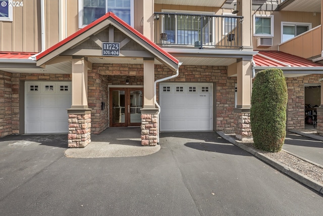 property entrance featuring driveway, board and batten siding, a balcony, stone siding, and an attached garage