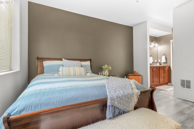 bedroom featuring wood finished floors, visible vents, and ensuite bath