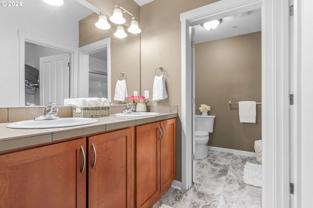 full bathroom with double vanity, toilet, marble finish floor, and a sink