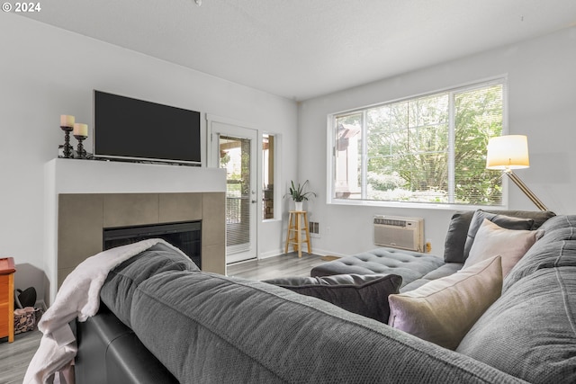 living room featuring wood finished floors, plenty of natural light, a wall unit AC, and a tiled fireplace