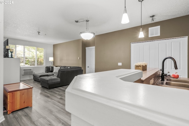 kitchen with a sink, a wall mounted air conditioner, visible vents, light wood-style flooring, and hanging light fixtures