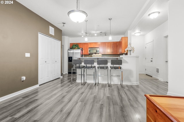 kitchen featuring light wood-type flooring, visible vents, appliances with stainless steel finishes, a breakfast bar area, and a peninsula