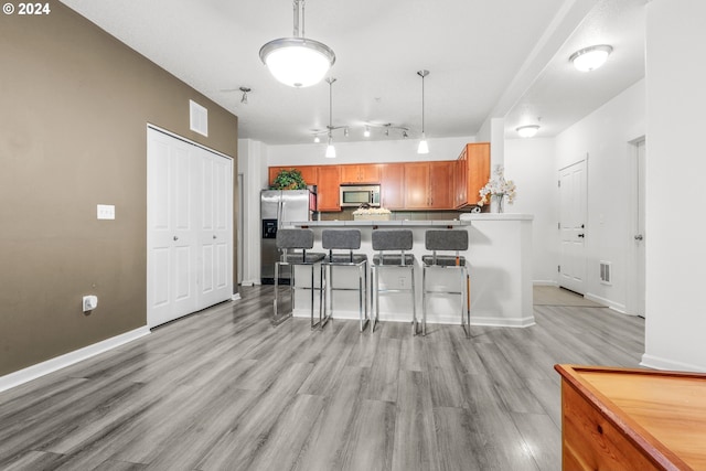 kitchen featuring a breakfast bar area, appliances with stainless steel finishes, light wood-type flooring, visible vents, and a peninsula