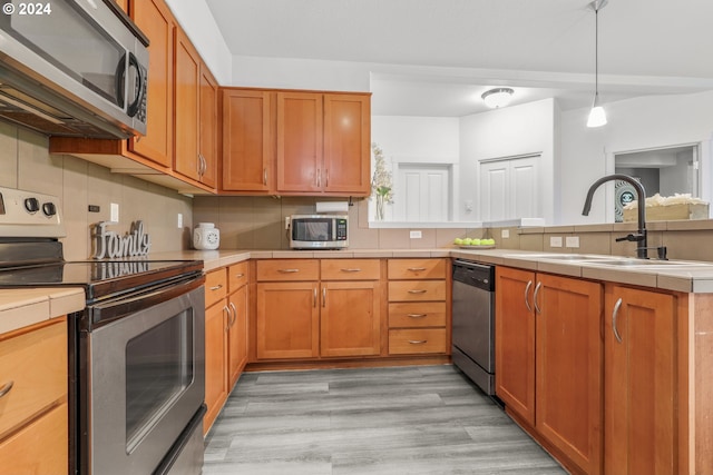 kitchen with light wood-type flooring, decorative backsplash, a peninsula, stainless steel appliances, and a sink