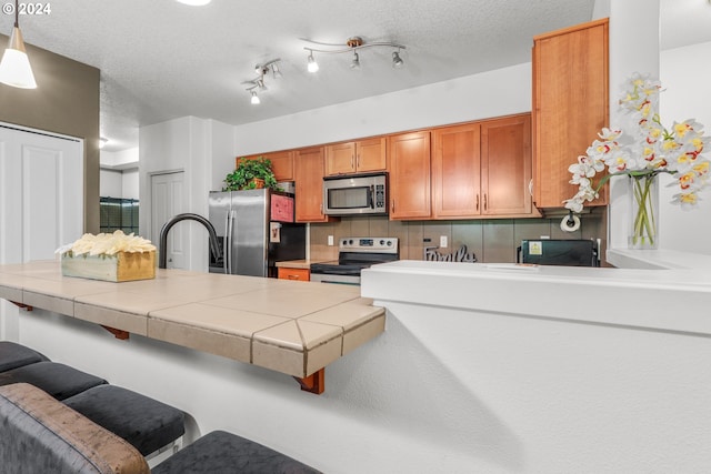 kitchen featuring tile counters, a breakfast bar area, brown cabinets, stainless steel appliances, and a textured ceiling