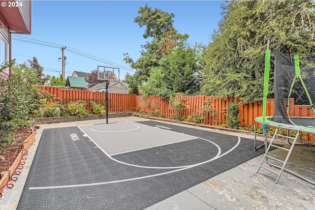 view of basketball court featuring a trampoline, a fenced backyard, and basketball hoop