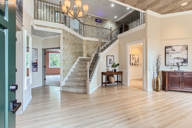 foyer with ornamental molding, a towering ceiling, and light wood finished floors