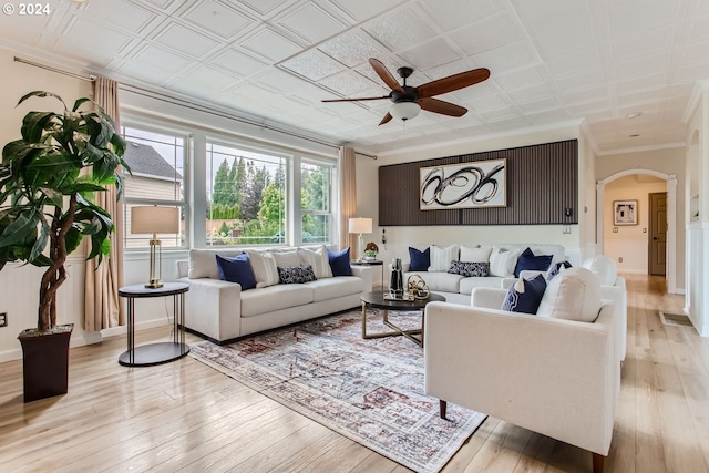 living area with light wood finished floors, arched walkways, a ceiling fan, an ornate ceiling, and crown molding