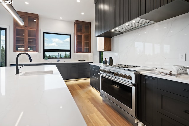 kitchen featuring range with two ovens, sink, light wood-type flooring, light stone counters, and tasteful backsplash