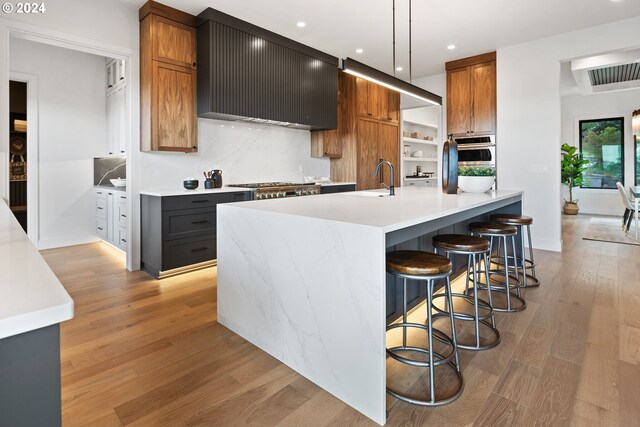 kitchen with wall chimney range hood, hanging light fixtures, sink, light wood-type flooring, and appliances with stainless steel finishes