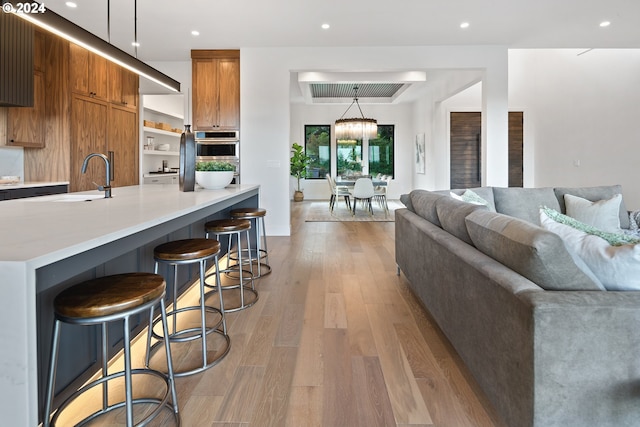 kitchen with oven, sink, a kitchen breakfast bar, hanging light fixtures, and light hardwood / wood-style flooring