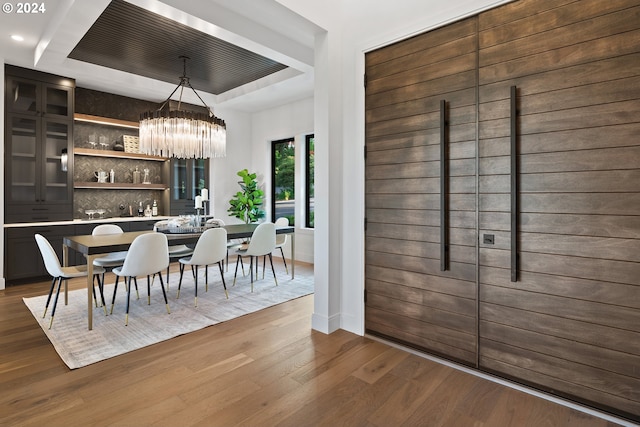 dining space with a tray ceiling, wood-type flooring, and an inviting chandelier