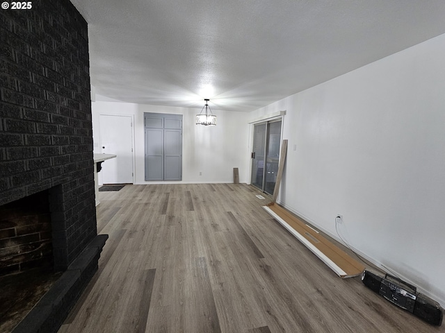 unfurnished living room featuring light wood finished floors, a brick fireplace, a notable chandelier, and a textured ceiling