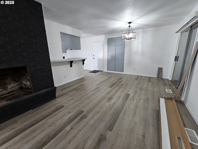 unfurnished living room featuring visible vents, baseboards, wood finished floors, a brick fireplace, and a notable chandelier