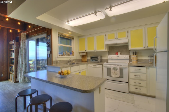 kitchen featuring white cabinetry, sink, kitchen peninsula, white appliances, and a kitchen bar