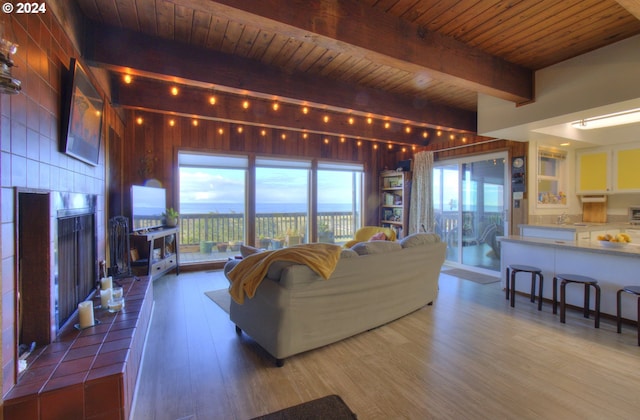 living room featuring a tile fireplace, wood-type flooring, beam ceiling, and wood ceiling