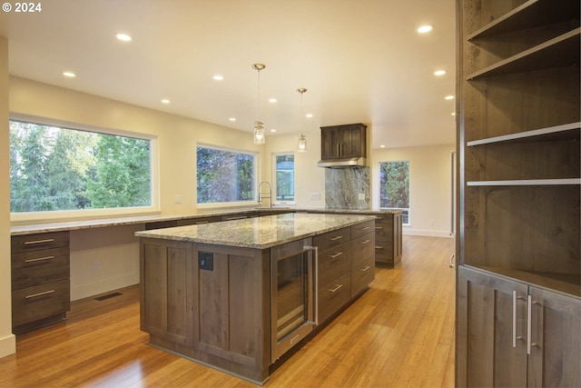 kitchen with dark brown cabinets, wine cooler, hanging light fixtures, light stone counters, and a kitchen island