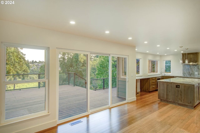 kitchen with light wood-type flooring, light stone counters, pendant lighting, and sink