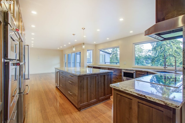 kitchen with light hardwood / wood-style floors, light stone countertops, pendant lighting, and a kitchen island