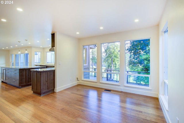 kitchen featuring light wood-type flooring, dark brown cabinetry, hanging light fixtures, and light stone counters