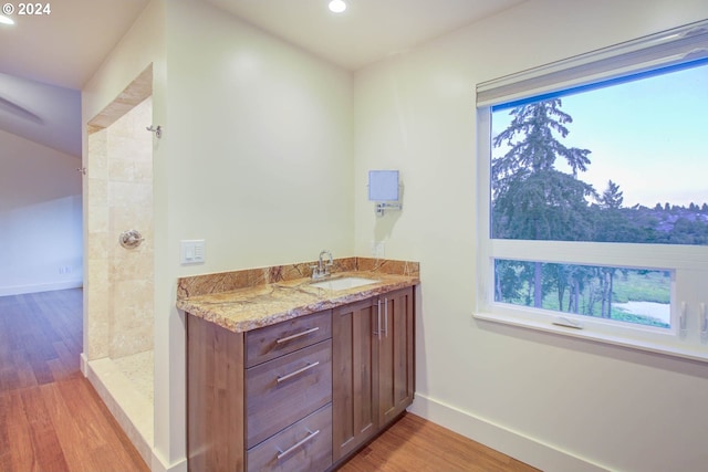 bathroom with hardwood / wood-style floors, tiled shower, and vanity