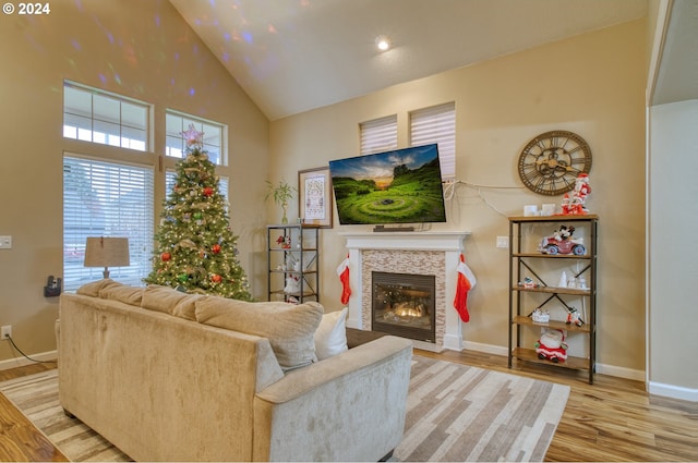 living room featuring a stone fireplace, high vaulted ceiling, and light hardwood / wood-style flooring