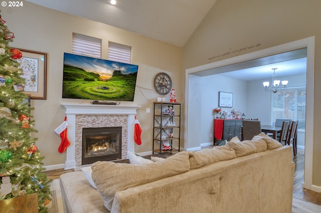 living room with an inviting chandelier, a stone fireplace, lofted ceiling, and light hardwood / wood-style flooring