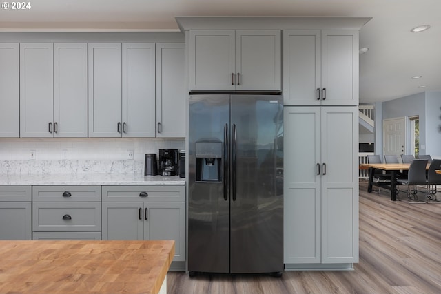 kitchen with light hardwood / wood-style flooring, butcher block counters, stainless steel refrigerator with ice dispenser, decorative backsplash, and gray cabinets