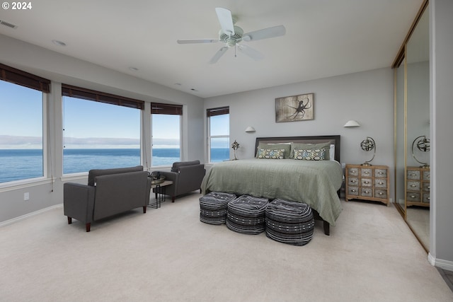 carpeted bedroom featuring ceiling fan, a water view, and multiple windows