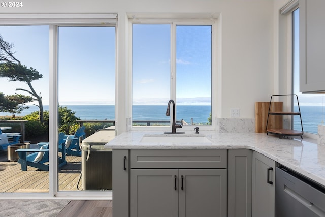 kitchen with sink, light stone countertops, gray cabinetry, and a water view