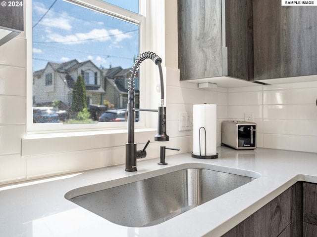 room details featuring dark brown cabinetry, decorative backsplash, and sink