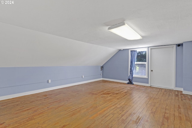 additional living space featuring light hardwood / wood-style flooring, vaulted ceiling, and a textured ceiling