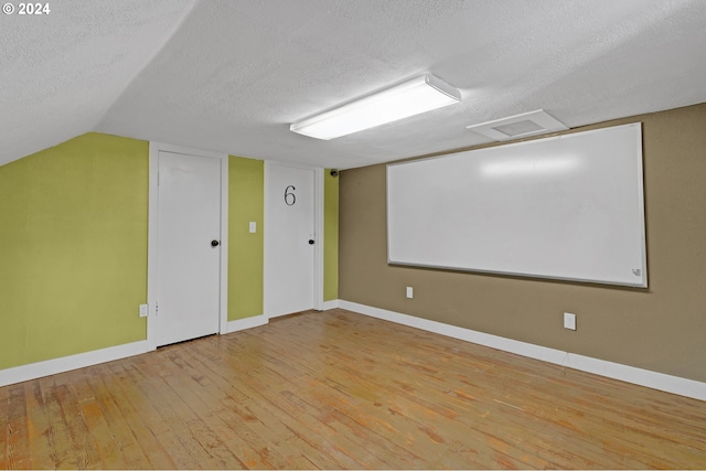 additional living space with light hardwood / wood-style flooring, vaulted ceiling, and a textured ceiling