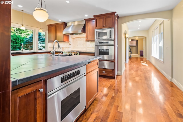 kitchen featuring appliances with stainless steel finishes, light wood-type flooring, wall chimney range hood, and plenty of natural light