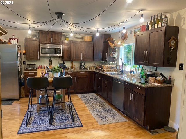 kitchen with appliances with stainless steel finishes, decorative light fixtures, sink, light hardwood / wood-style floors, and dark brown cabinets