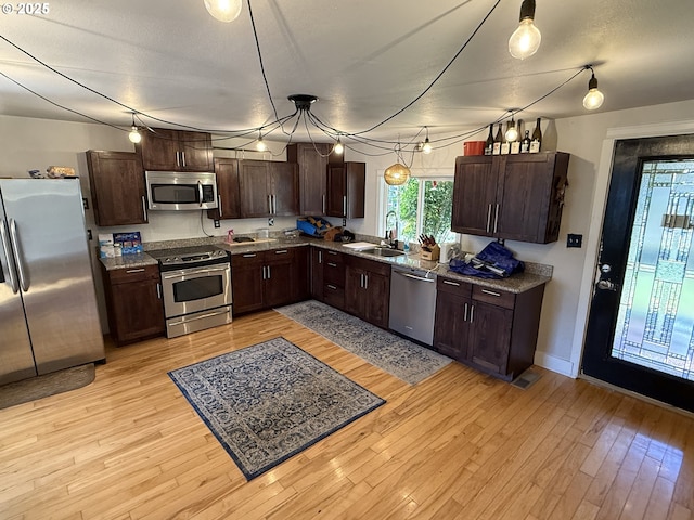 kitchen with stainless steel appliances, sink, hanging light fixtures, and light wood-type flooring